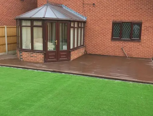 Brown composite decking along a conservatory with a new artificial grass lawn