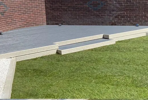 Grey composite decking with a low step down onto a freshly laid lawn