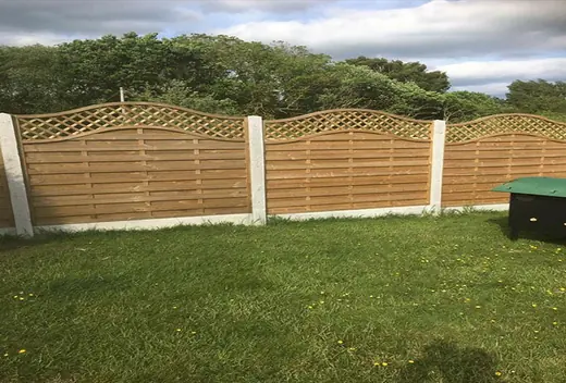 Timber fence panels with arched trellis tops fitted between concrete posts and gravel boards