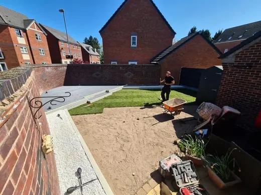 STL team member mid-build on a new garden with grey composite decking, fresh turf and a white chipping path