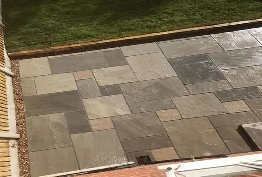 Grey natural stone patio laid in a random pattern, edged with a timber sleeper against the lawn