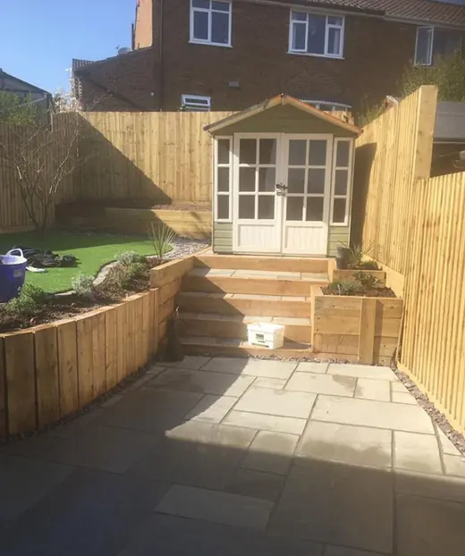 Tiered timber sleeper retaining walls with sleeper steps leading up to a summerhouse above a slab patio